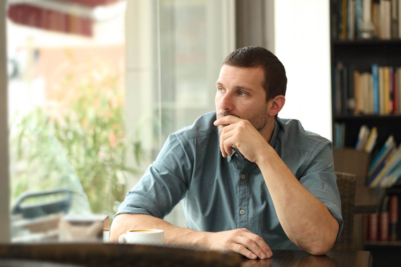 A man sitting at a cafe table, looking out a window
